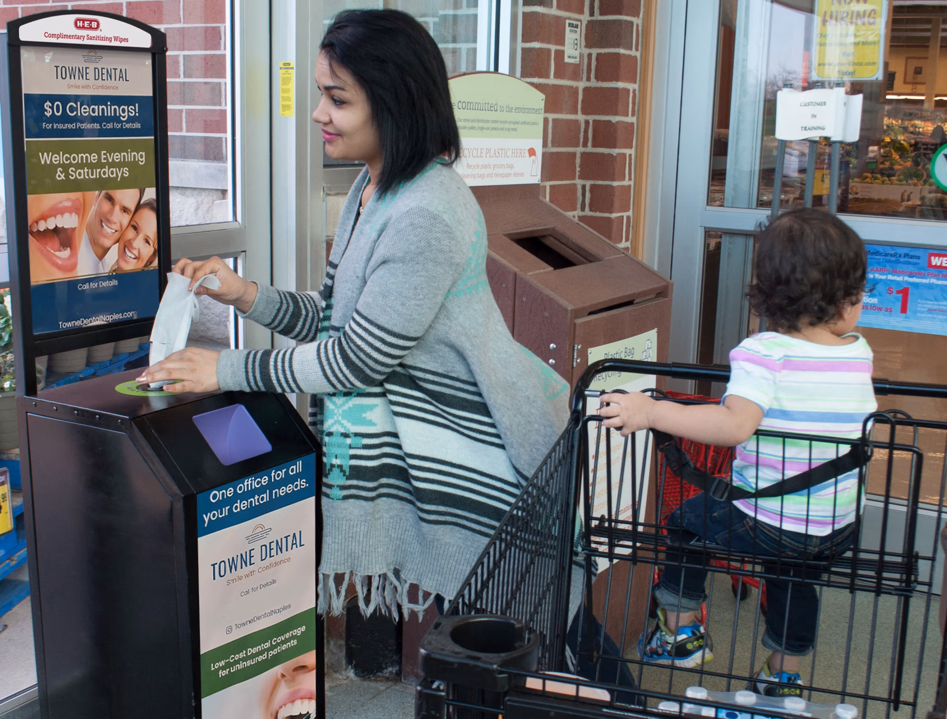 Woman viewing a Terraboost wellness kiosk with a dentist ad, with child in her grocery basket